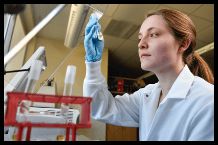 A female research graduate student studies the contents of a beaker. 