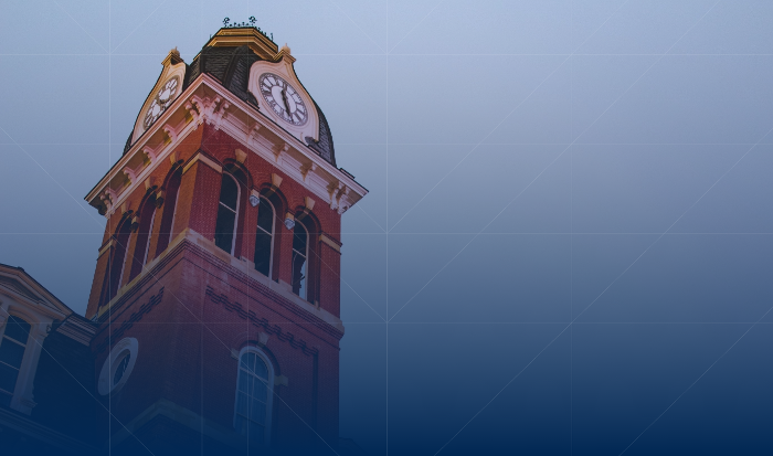 A red-brick clock tower against a blue gradient background. the tower features a golden clock and a peaked roof.