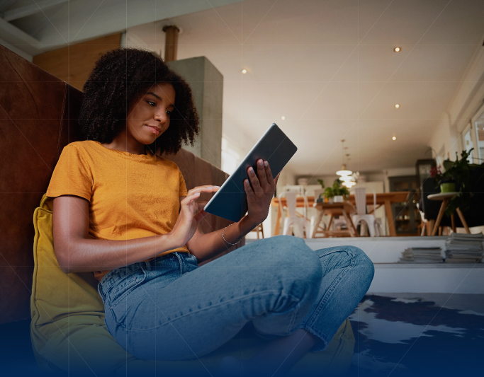 A woman sitting on a couch, wearing a yellow shirt and jeans, looks at a tablet in a modern living room.